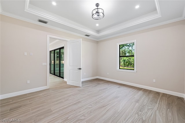 spare room featuring a tray ceiling, crown molding, and light wood-type flooring