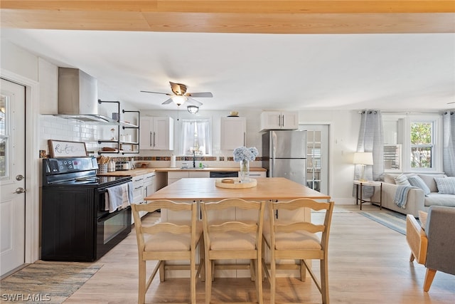 kitchen with light wood-type flooring, stainless steel fridge, ceiling fan, black / electric stove, and white cabinets