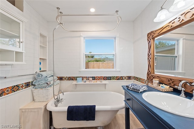 bathroom featuring hardwood / wood-style floors, tile walls, vanity, and a tub