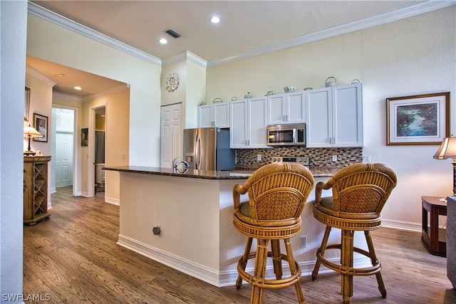 kitchen with hardwood / wood-style floors, white cabinetry, appliances with stainless steel finishes, and a breakfast bar area