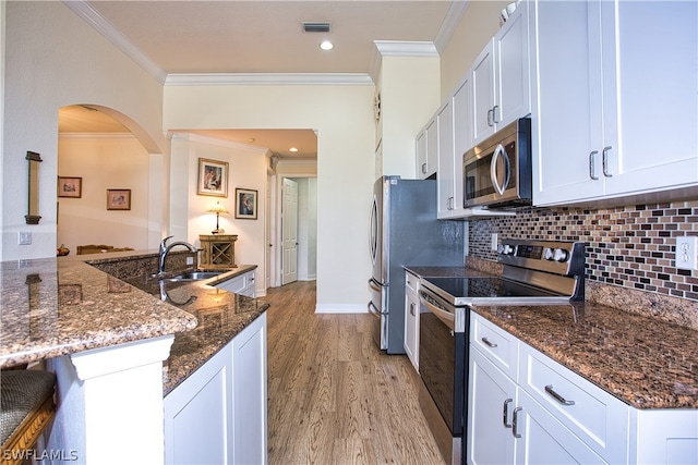 kitchen featuring sink, dark stone counters, white cabinets, stainless steel appliances, and backsplash