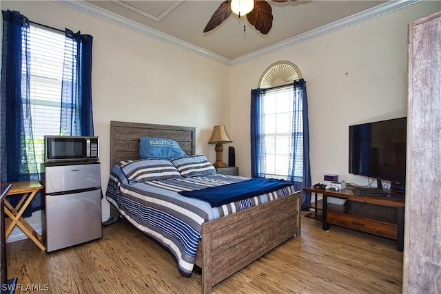 bedroom with stainless steel refrigerator, ceiling fan, wood-type flooring, and multiple windows