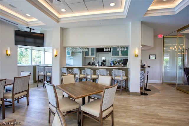 dining space featuring a towering ceiling, a tray ceiling, and light hardwood / wood-style flooring