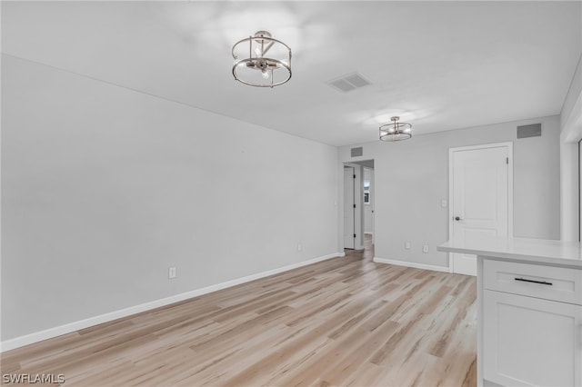 empty room with light hardwood / wood-style flooring and an inviting chandelier