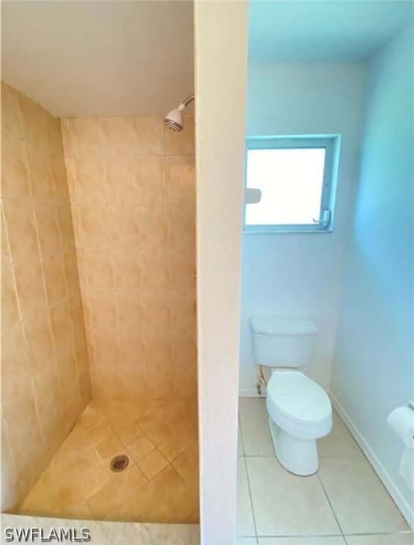 bathroom featuring tile flooring, tiled shower, and toilet