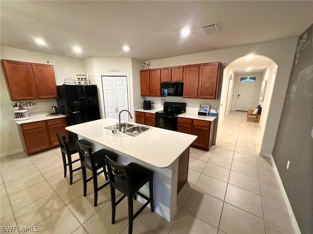 kitchen with light tile patterned floors, sink, black appliances, a kitchen breakfast bar, and a kitchen island with sink