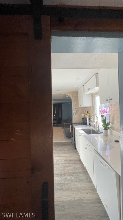 kitchen with backsplash, white dishwasher, white cabinets, sink, and light wood-type flooring