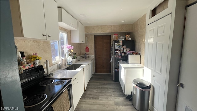 kitchen with white cabinets, sink, black fridge, dark hardwood / wood-style floors, and range with electric stovetop