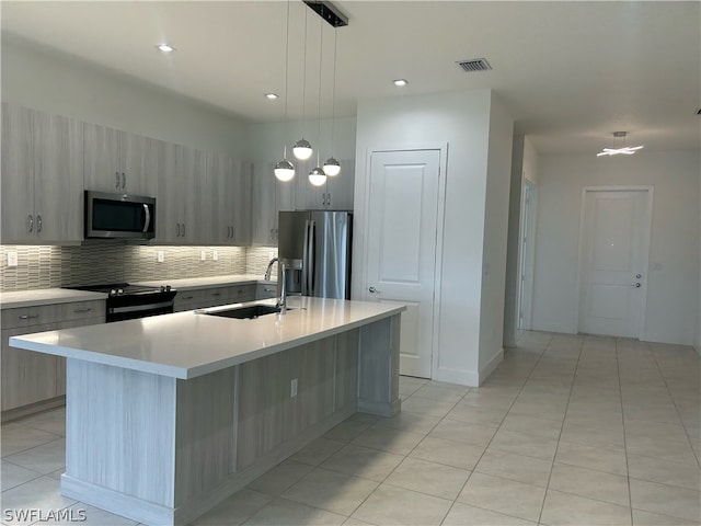 kitchen featuring hanging light fixtures, stainless steel appliances, an island with sink, sink, and tasteful backsplash