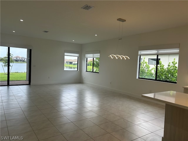 empty room featuring a healthy amount of sunlight, a water view, and light tile floors