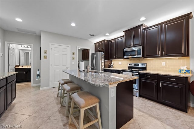 kitchen with a kitchen island with sink, sink, appliances with stainless steel finishes, light tile patterned flooring, and a breakfast bar area