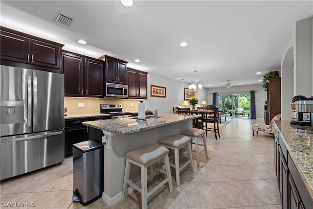 kitchen with a kitchen island with sink, a kitchen breakfast bar, decorative backsplash, light tile patterned floors, and stainless steel appliances