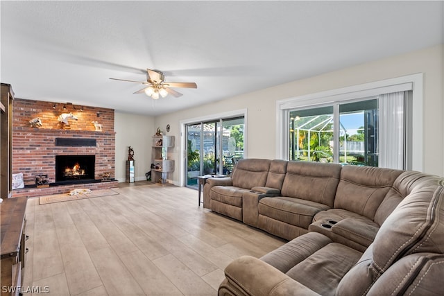 living room featuring a fireplace, ceiling fan, light wood-type flooring, and brick wall