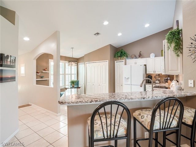 kitchen with a breakfast bar area, vaulted ceiling, white fridge with ice dispenser, light stone counters, and white cabinets