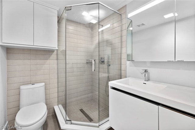 bathroom with tile walls, toilet, vanity, and an enclosed shower