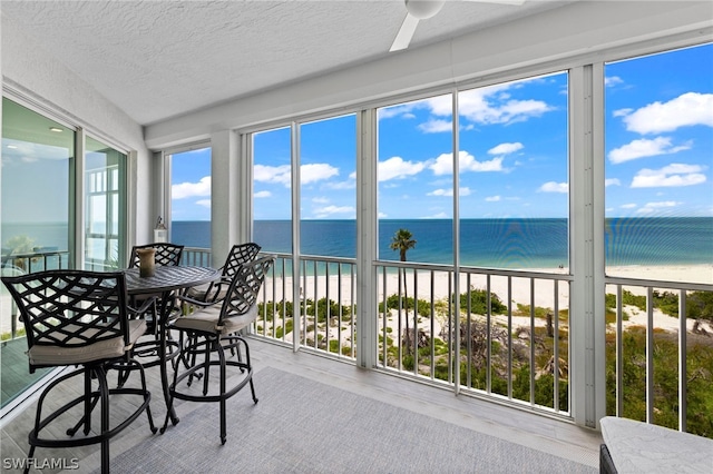 sunroom with a view of the beach, a water view, and ceiling fan