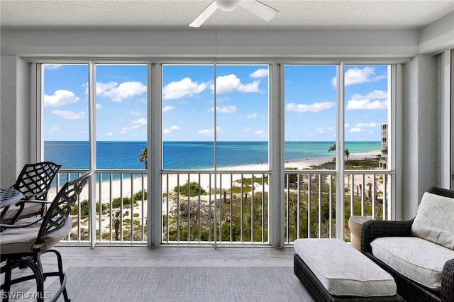 sunroom / solarium featuring a view of the beach, a water view, ceiling fan, and plenty of natural light