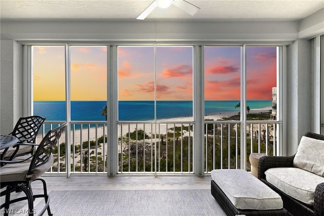 sunroom featuring a water view, ceiling fan, and a beach view