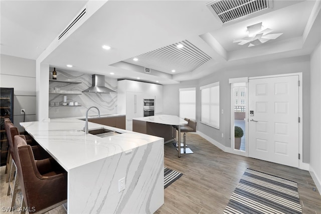 kitchen with a breakfast bar, a raised ceiling, and wall chimney range hood