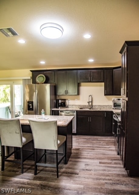 kitchen with sink, appliances with stainless steel finishes, a kitchen island, a kitchen breakfast bar, and hardwood / wood-style floors