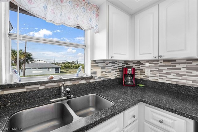 kitchen with tasteful backsplash, white cabinetry, dark stone counters, and a sink