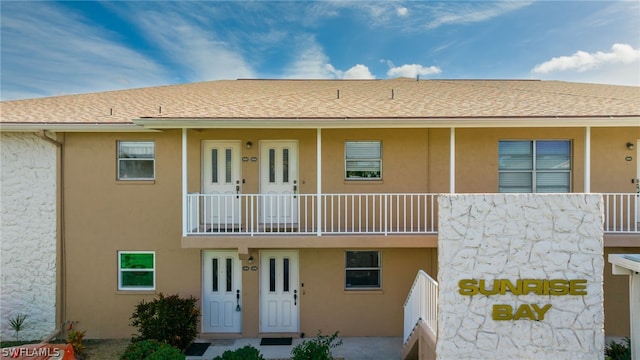 exterior space with stucco siding, a balcony, and a shingled roof