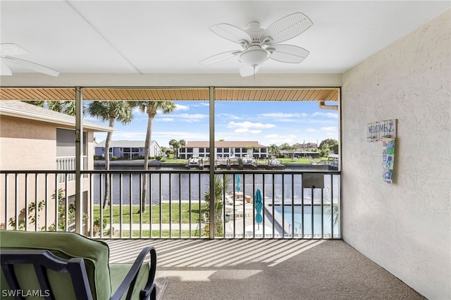 sunroom with ceiling fan and a water view