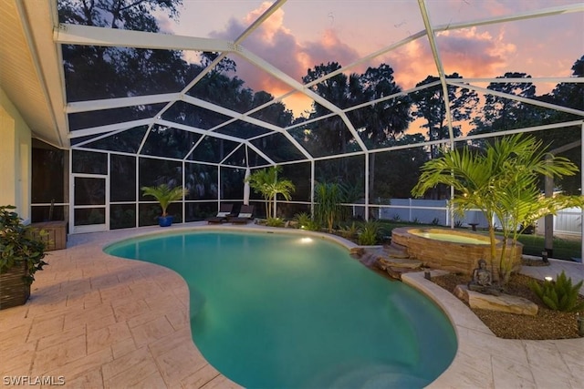 pool at dusk with glass enclosure, an in ground hot tub, and a patio area