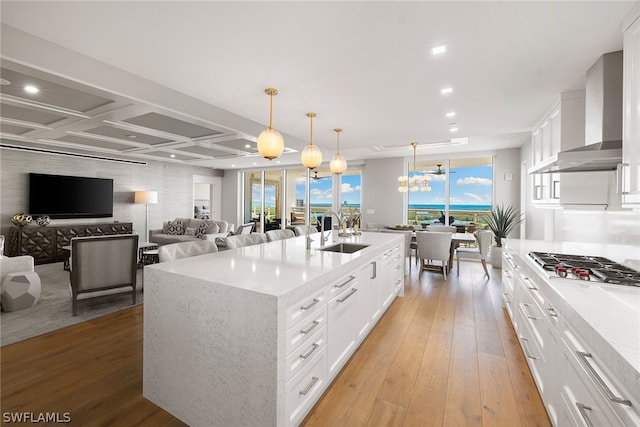 kitchen featuring light hardwood / wood-style floors, wall chimney range hood, a kitchen island with sink, sink, and coffered ceiling