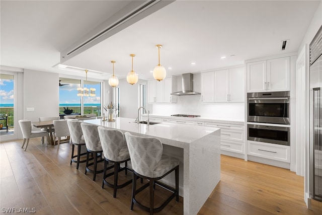 kitchen with light hardwood / wood-style floors, white cabinets, wall chimney exhaust hood, stainless steel double oven, and sink