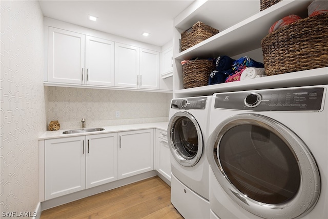 washroom featuring light hardwood / wood-style floors, sink, washing machine and dryer, and cabinets