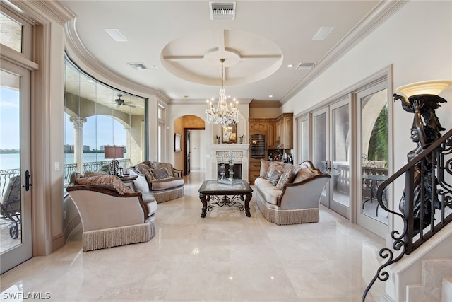 living room featuring a water view, light tile floors, ceiling fan with notable chandelier, a raised ceiling, and ornamental molding