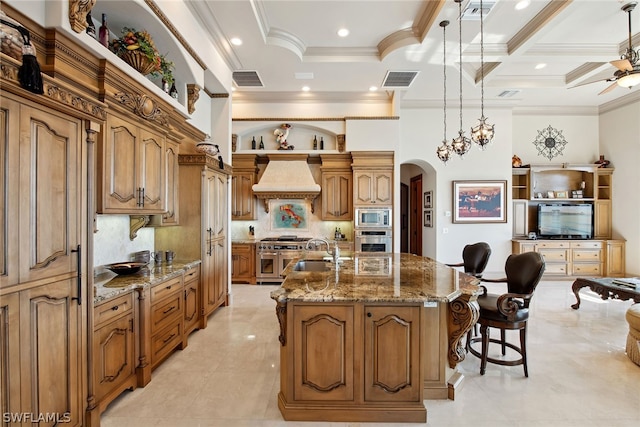 kitchen featuring appliances with stainless steel finishes, ceiling fan, a center island with sink, custom range hood, and a kitchen breakfast bar