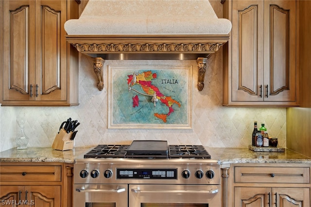 kitchen with light stone counters, range with two ovens, backsplash, and premium range hood