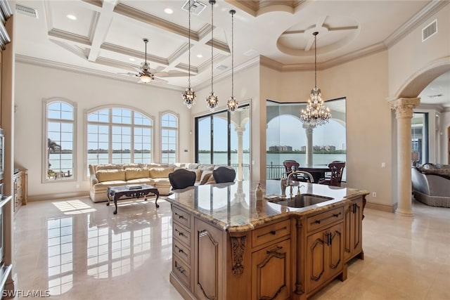 kitchen with ceiling fan with notable chandelier, coffered ceiling, an island with sink, light stone counters, and light tile floors