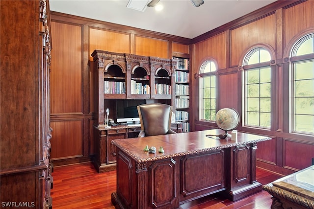 home office with ceiling fan, plenty of natural light, dark wood-type flooring, and wooden walls