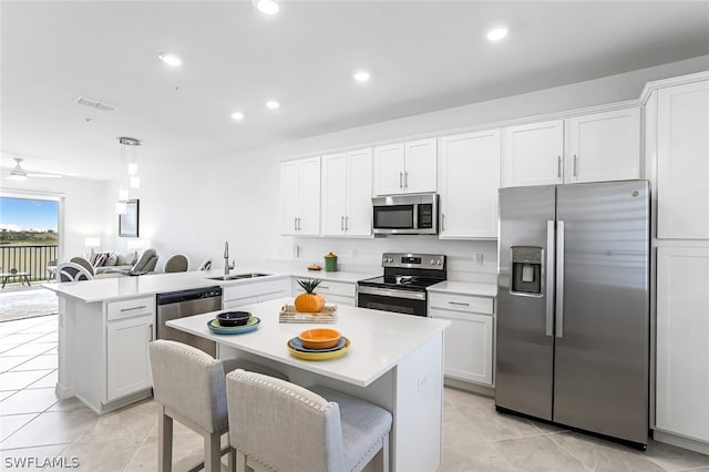 kitchen with a peninsula, a sink, white cabinets, light countertops, and appliances with stainless steel finishes