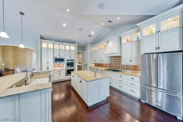 kitchen featuring premium range hood, a center island with sink, vaulted ceiling, decorative light fixtures, and stainless steel appliances