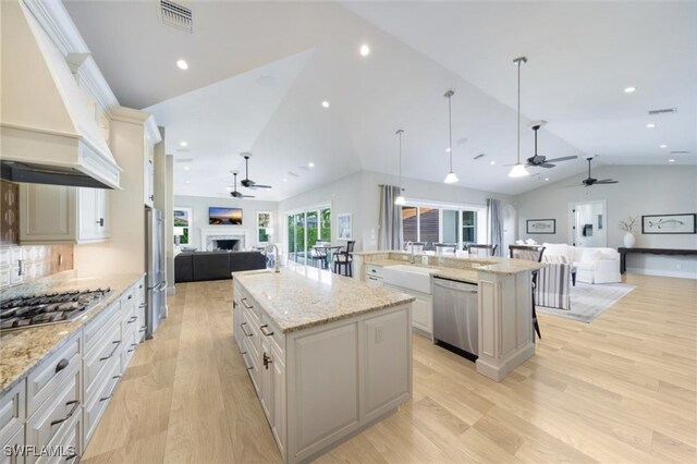 kitchen featuring pendant lighting, lofted ceiling, a large island with sink, light hardwood / wood-style flooring, and appliances with stainless steel finishes