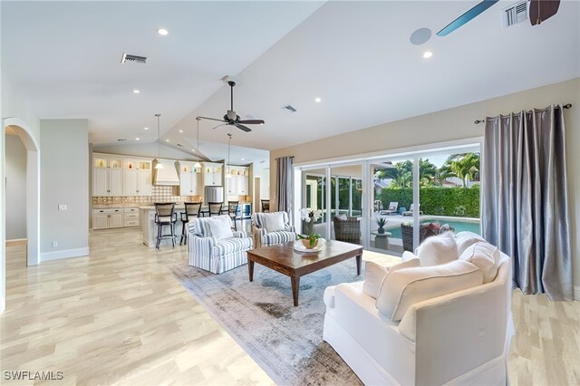 living room with ceiling fan, vaulted ceiling, and light wood-type flooring