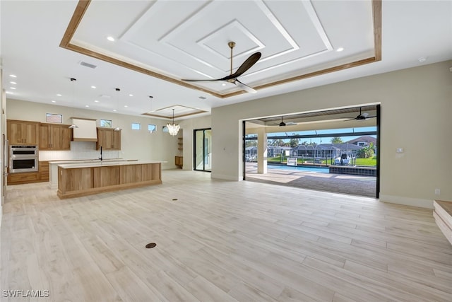 unfurnished living room featuring a tray ceiling, ceiling fan with notable chandelier, and light wood-type flooring