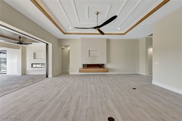 unfurnished living room with a tray ceiling, a tiled fireplace, ceiling fan, and light wood-type flooring