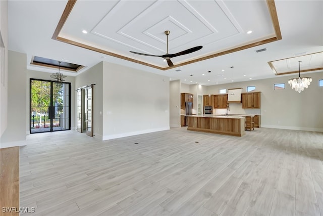 unfurnished living room with ceiling fan with notable chandelier, a raised ceiling, sink, and light hardwood / wood-style flooring