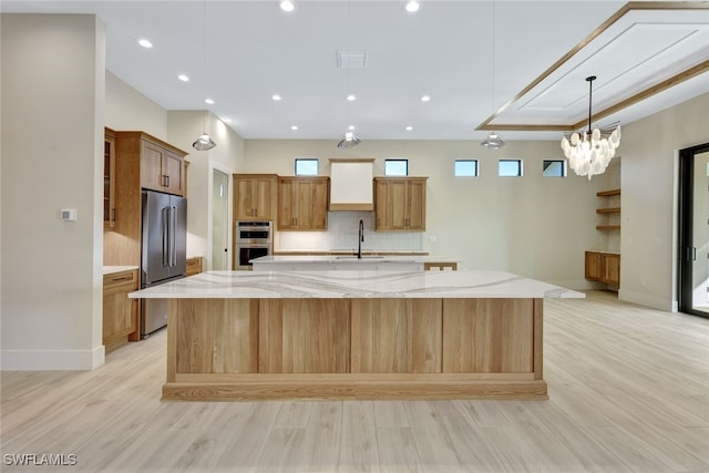 kitchen with pendant lighting, a spacious island, light stone countertops, light wood-type flooring, and stainless steel appliances