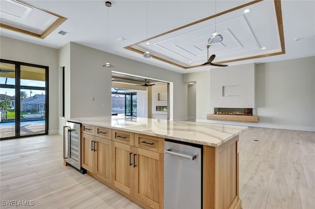 kitchen featuring hanging light fixtures, light wood-type flooring, a raised ceiling, and beverage cooler