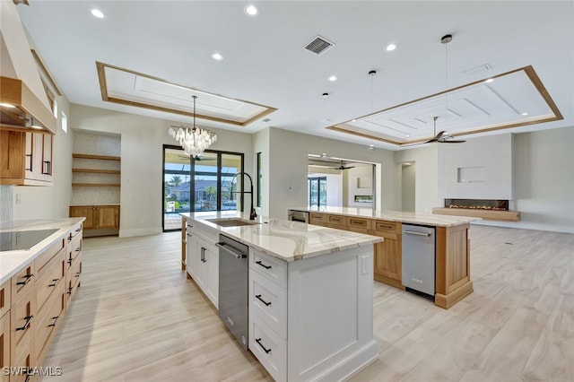 kitchen featuring white cabinets, a large island, ceiling fan with notable chandelier, and a tray ceiling