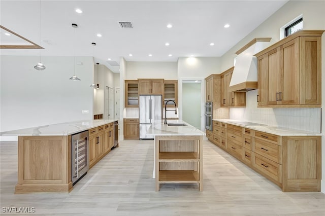 kitchen featuring custom range hood, stainless steel appliances, beverage cooler, a large island with sink, and hanging light fixtures