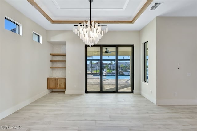 unfurnished room with light hardwood / wood-style floors, a raised ceiling, and a chandelier