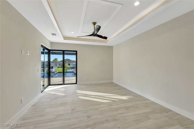 spare room featuring ceiling fan, light hardwood / wood-style floors, a water view, and a tray ceiling