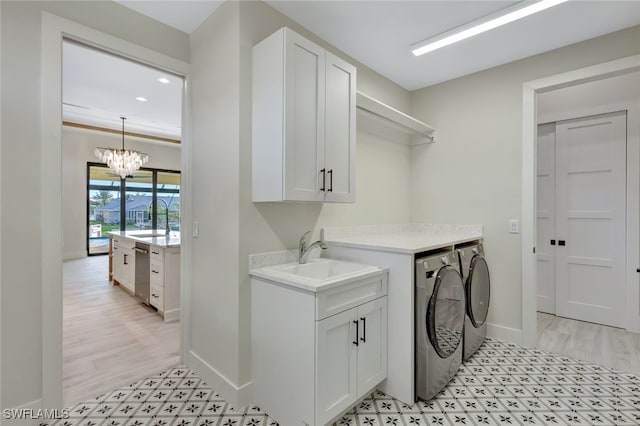 laundry area featuring cabinets, sink, light wood-type flooring, a notable chandelier, and washing machine and clothes dryer